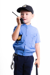 Cute little police boy with smile on face and baton on white background. Intelligent cool children in police suit with blue eyes and baton use radio walkie talkie