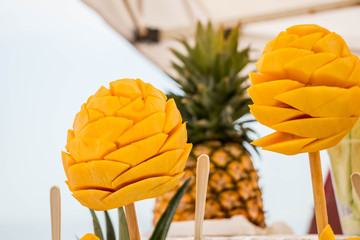 Mangos en palito, bocadillo típic Mexicano, con una piña en segundo plano al fondo.