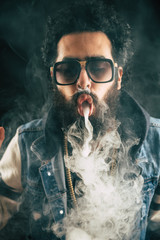 Young man with beard throwing a cloud of steam. Black background. Vaping an electronic cigarette...