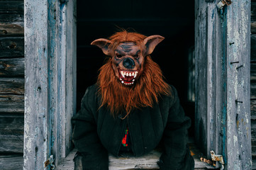 Unknown person with creepy horrible werewolf mask looking out from old wooden ghost house window. Helloween concept.  Spooky terrible fearful monster. Children fear. Frightening tales. Nightmare.