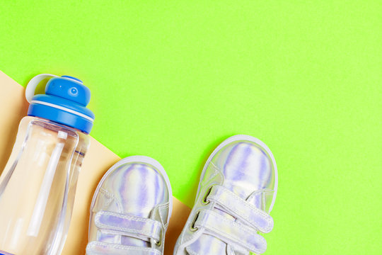 Child sneakers and bottle of water on green background.
