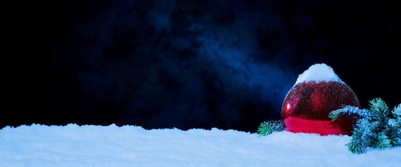 Weihnachtskugel mit Tannenzweig im Schnee vor tiefblauem Hinterdrund