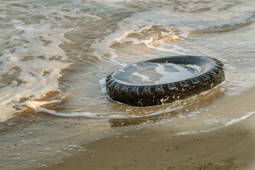 Old black rubber tire left on beach, environment pollution concept, selective focus, color toned...