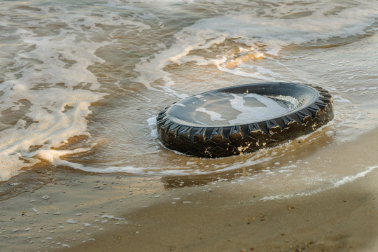 Old black rubber tire left on beach, environment pollution concept, selective focus, color toned picture. Discarded old tyre in blue water on beach. Pollutions and garbages in sea and on beach
