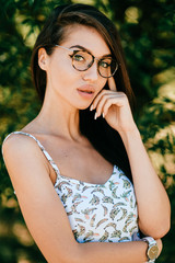 Fototapeta premium Closeup emotional lifestyle portrait of adorable beautiful young cheerful coquette fashionable girl in trendy glasses with big natural lips and blue happy eyes smiling outdoor at nature in summer.
