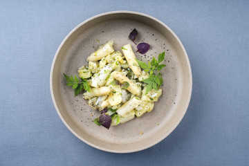 Modern style traditional German potato salad with white asparagus and gherkin as close up on a plate with copy space
