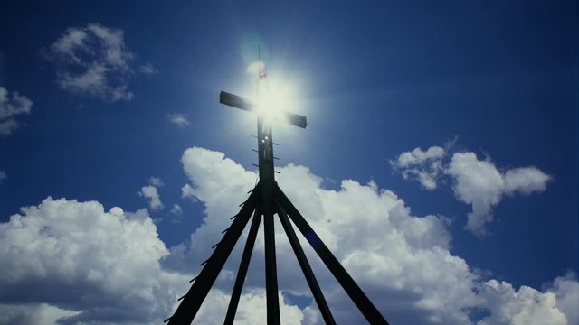 Cross and sun with moving white clouds against blue sky.