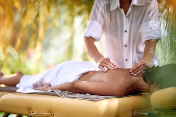 woman is relaxing in spa and wellness center while receiving massage in nature.
