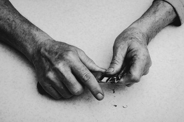 Elderly man sharpens pencil with clerical knife. Hands of old man close up in grayscale. Monochrome...