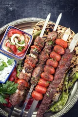 Fototapeten Traditional oriental Adana kebap and shashlik skewer with tomato and flatbread as top view on a plate © HLPhoto