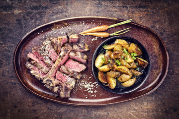 Barbecue dry aged wagyu porterhouse steak sliced with fried potatoes as top view on a plate