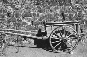 Fototapeta na wymiar Old wooden carriage on the ground and stone wall at background. Black and white.