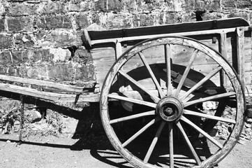 Fototapeta na wymiar Old wooden carriage on the ground and stone wall at background. Black and white photo.