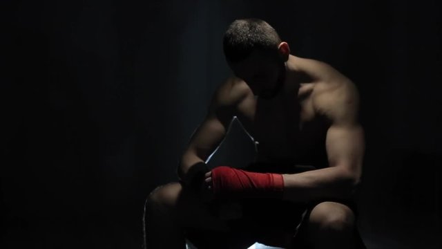 A disappointed young strong male sportsman sitting and looking down. An upset boxer after the failure