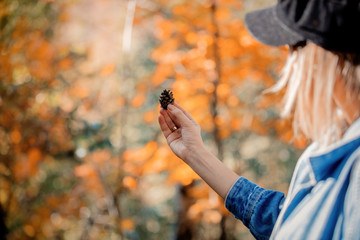 Girl holding a little pine cone on forest background. Autumn season time