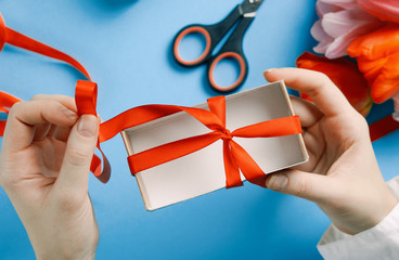 Female hands are holding a gift before wrapping near tulip flowes on blue background