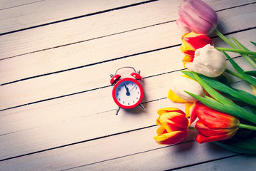 Beautiful bouquet of tulips and clock on white wooden background