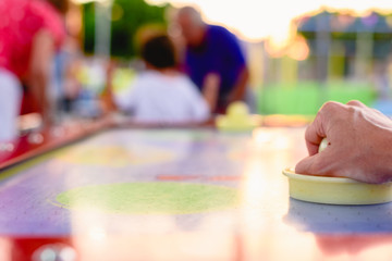 Hand holding a stick to hit disc in the table air hockey game.