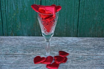glass goblet with red hearts on a gray wooden table against a green wall