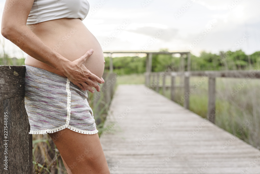 Wall mural Close-up of pregnant woman's belly stroking with her hands in nature.