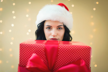 Young woman with santa hat holding a gift box on a shiny light background