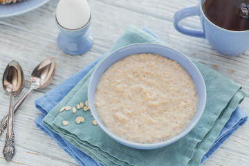 Oatmeal porridge bowl on the white wooden background.