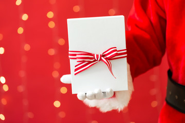 Santa holding a Christmas gift on a shiny light red background