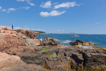 Tourists on rocky red shore at Acadia National Park