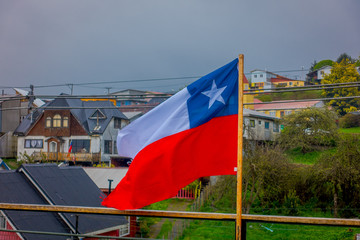 Outdoor view of Chilean flag waving with beautiful and colorful houses on stilts palafitos behind in the horizont in Castro, Chiloe Island