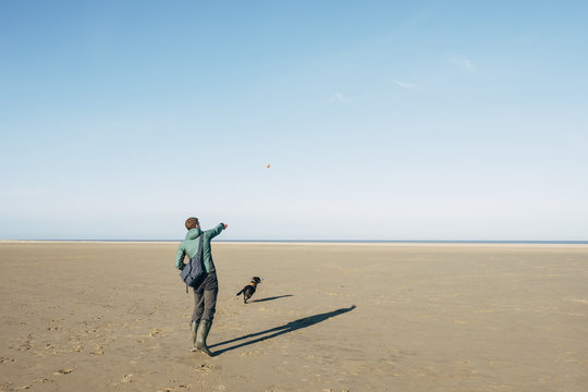 Male playing ball with his dog on a vast empty beach. Holkham, N