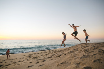 Energetic dad playing with kids on the beach at sunset