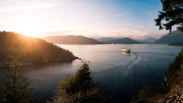 A ferry ship cruising out of a harbour in a mountain pass at sunset