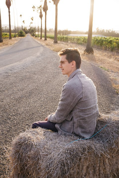 young male sitting on bails of hay in california sun