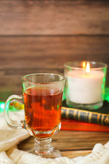 Cozy winter still life: cup of hot tea and books, candle on wooden background and blurred garland lights