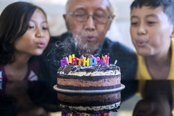 Old man and grandchildren blow birthday candles