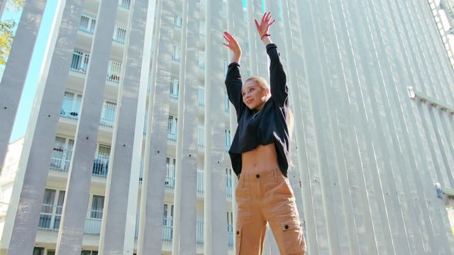 A young girl performs modern hip hop dance on the streets of the city during the summer, twisting and rotating.