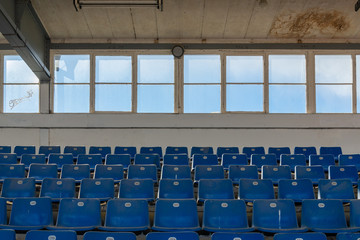 Naklejka premium Front view row of blue plastic seats on rough concrete step floor in old vintage dirty concrete structural stadium with windows frame background without people. 