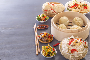 Chinese food on a gray wooden table. Traditional steamed dumplings, noodles, vegetables, seafood. Copy space