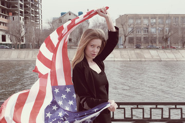 Instagram sutro style image of blond women with weaving stars and stripes in her hands near river fence in city with copyspace.