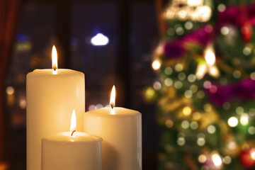 Three white candles with blurred Christmas tree