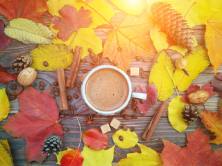 Fototapeta na wymiar A hot cup of coffee on a wooden table with autumn leaves and spices