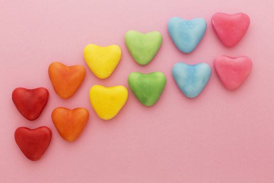 Heart-shaped multi-colored candy ordered in rainbow colors and shape on a pink background