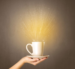 Young female hand holding tea mug with a beam of light rising out of it