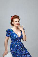 Studio shot of amazed beautiful young retro model with vintage hairdo and red lipstick holding hand at mouth, expressing full disbelief, surprised with unexpected astonishing news. Rockabilly style