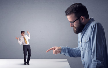Young professional businessman being angry with an other miniature businessman in front of a grey...