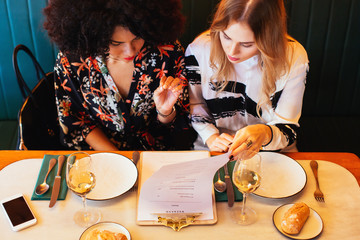 Overhead of female friends looking a menu in restaurant.