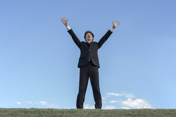 Fototapeta na wymiar 青空をバックに空に向かい手を広げる若い男性1人。成功・勝者・パワー・挑戦イメージ