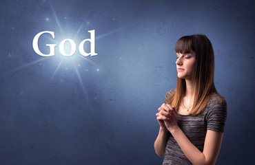 Obraz premium Young woman praying on a blue background with the word God written above her