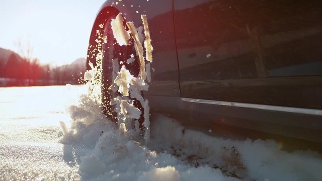 SLOW MOTION, CLOSE UP, LENS FLARE: Black rubber tyre on the wheel of a powerful car losing traction in the fresh snow. Cool shot of four wheel drive car driving off road in the slippery wet snow.