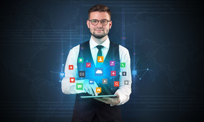 Handsome businessman in suit with tablet on his hand and application icons above
